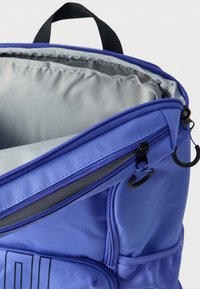 Μωβ σακίδιο πλάτης κατασκευασμένο από ανθεκτικό ύφασμα, με γκρι εσωτερική επένδυση, κλείσιμο με φερμουάρ και μαύρες μεταλλικές λεπτομέρειες. Διαθέτει πλάγια τσέπη από δίχτυ.