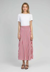 Jupe maxi à rayures verticales rouges et blanches, taille haute, en tissu doux, associée à un t-shirt blanc uni et des sandales noires à lanières.