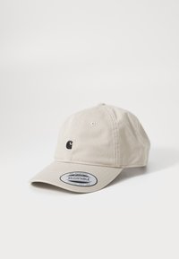 Justerbar beige bomullslue med en liten svart logo på forsiden og en rund justerbar stropp på baksiden.