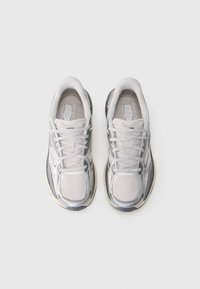 Baskets de sport gris clair en mesh, avec des superpositions texturées, des lacets plats et une semelle rembourrée. Présente des accents réfléchissants sur le design.