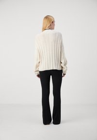 Krämfärgad stickad tröja med ribbat mönster, oversized passform och elastiska ärmslut. Kombinerad med svarta vida byxor och minimala accessoarer.