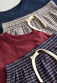 Tre föremål: en marinblå sweatshirt, en vinröd topp och rutiga pyjamasbyxor med en beige dragsko. Mjuk tyg, ribbade kragar och detaljerade mönster.