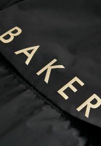 Črn material z gladko teksturo, ki vsebuje velika, krepka zlata črka, ki črkuje "BAKER." Material ima zbrano robno podrobnost.