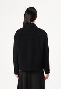 Schwarze Jeansjacke mit lockerer Passform, Knopfmanschetten und einfachem Kragen. Die Rückseite hat ein schlichtes Design ohne Verzierungen.