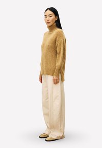 Beige coltrui van zachte, getextureerde stof, gecombineerd met roomkleurige broek met brede pijpen. Neutrale slip-on schoenen maken de outfit compleet.