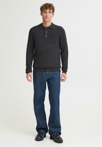 Mørkegrå strikket genser med polo-krage, som har tre knapper og teksturert stoff, kombinert med blå rette jeans og svarte sko.