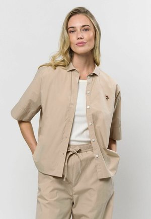 Beige kortærmet skjorte med knapper lavet af letvægtsstof, med en subtil tekstureret overflade og en lille blomsterbroderi detalje på brystet.