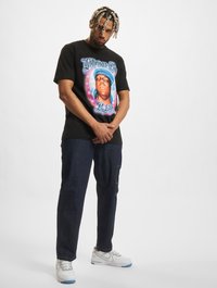 Melnas kokvilnas T-krekls ar krāsainu grafisku attēlu, kurā attēlots vīrieša figūra ar uzrakstu "The Notorious B.I.G. R.I.P." stilizētā burtnīcā.