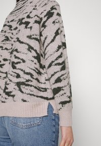 Gebreide trui in lichtroze met een donkergroen abstract patroon, met zijsplitten en een geribde hem. Draag met lichtblauwe denim.