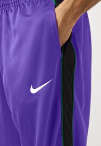 Fialové športové šortky s čiernymi bočnými panelmi, s bielym logom Nike. Vyrobené z hladkej tkaniny s jemným leskom a elastickým pásom.