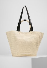 Spleciona torba na ramię z trawy w odcieniu kremowym, z czarnymi skórzanymi uchwytami. Charakteryzuje się szerokim otwartym wierzchem oraz teksturowaną powierzchnią z poziomymi przeszyciami.