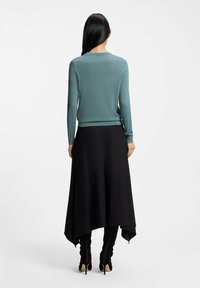 Licht turquoise, langärmelig top met geribbelde randen gecombineerd met een zwarte, asymmetrische rok. Zwarte hoge hakken maken de outfit af.