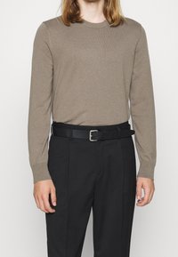 Beige pitkähihaisessa neuleessa, joka on valmistettu pehmeästä materiaalista, yhdistetty mustiin housuihin ja mustaan vyöhön, jossa on hopeinen solki.