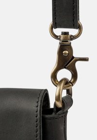 Close-up of black leather bag strap attached to brass swivel clasp and ring hardware.