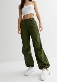 Volné kalhoty olivově zelené barvy s elastickým pasem a stahovací šňůrkou. Kombinované s bílými teniskami a krátkým bílým topem.