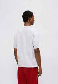 Γκρι κοντομάνικη μπλούζα με άνετη εφαρμογή και στρογγυλή λαιμόκοψη. Απαλό βαμβακερό υλικό, χωρίς ορατά σχέδια. Συνδυάζεται με κόκκινο παντελόνι.