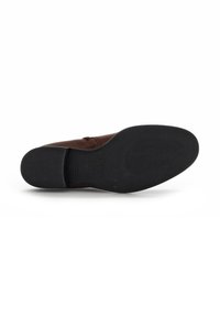 Chaussure en cuir brun avec un dessus lisse et une semelle en caoutchouc noir texturée. Le design comprend des coutures minimalistes et une forme de bout arrondi.