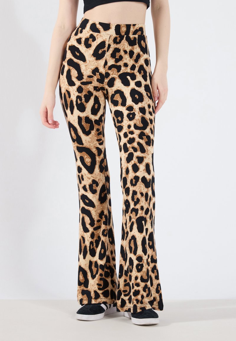 Hlače s leopard uzorkom u bež i crnoj boji, rebraste teksture; nosi se s crnim tenisicama, s visokim strukom i lepršavim siluetom.
