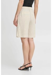 Shorts beige in lino con vita elasticizzata, design fino al ginocchio, due tasche posteriori e tessuto testurizzato. Indossati con sandali neri con tacco.