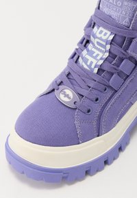 Sneaker in tela viola con tomaia testurizzata, suola in gomma bianca chunky e dettagli delle stringhe a contrasto. Presenta un'etichetta con il marchio sul lato.