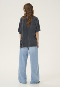 Sivý oversized tričko s klesnutými ramenami, kombinované s svetlomodrými širokými džínsami. Mäkka tkanina, minimalistický dizajn, bez viditeľných log.