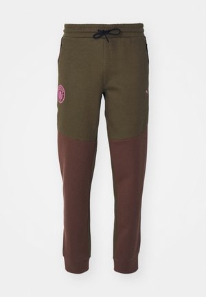 Olivgrüne und braune Sweatpants mit einem Kordelzugbund, Seitentaschen und einem rosa Logopatch am Oberschenkel. Weicher Stoff.