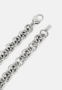 Sølvmetallkjedearmbånd med sammenkoblede runde lenker, med låsemekanisme og en liten tag gravert med "BOSS."