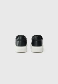 Zwarte leren sneakers met een witte zool, afgeronde vorm en een logodetail op de hak. Gladde textuur met een minimalistische stijl.