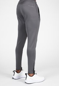 Grijze sportieve joggers met een slim fit, zijritschoenen en een logo op de achterkant, gecombineerd met witte sportschoenen met zwarte accenten.