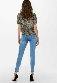 Top met luipaardprint met korte mouwen, lichtgekleurde denim skinny jeans en zwarte hoge hakken. Vervaagde blauwe jeans met rafelige zoomdetails.