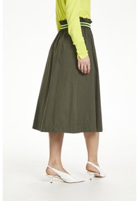 Falda verde oliva con una cinturilla alta y fruncida, y acentos en rayas negras y verdes. Un par de tacones tipo slingback blancos con un tacón bajo.