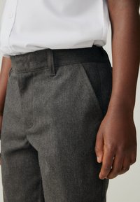 Dunkelgraue, maßgeschneiderte Hose mit glatter Textur, ausgestattet mit flacher Front, Seitentaschen und geradem Bein. Kombiniert mit einem weißen Hemd mit Knopfleiste.