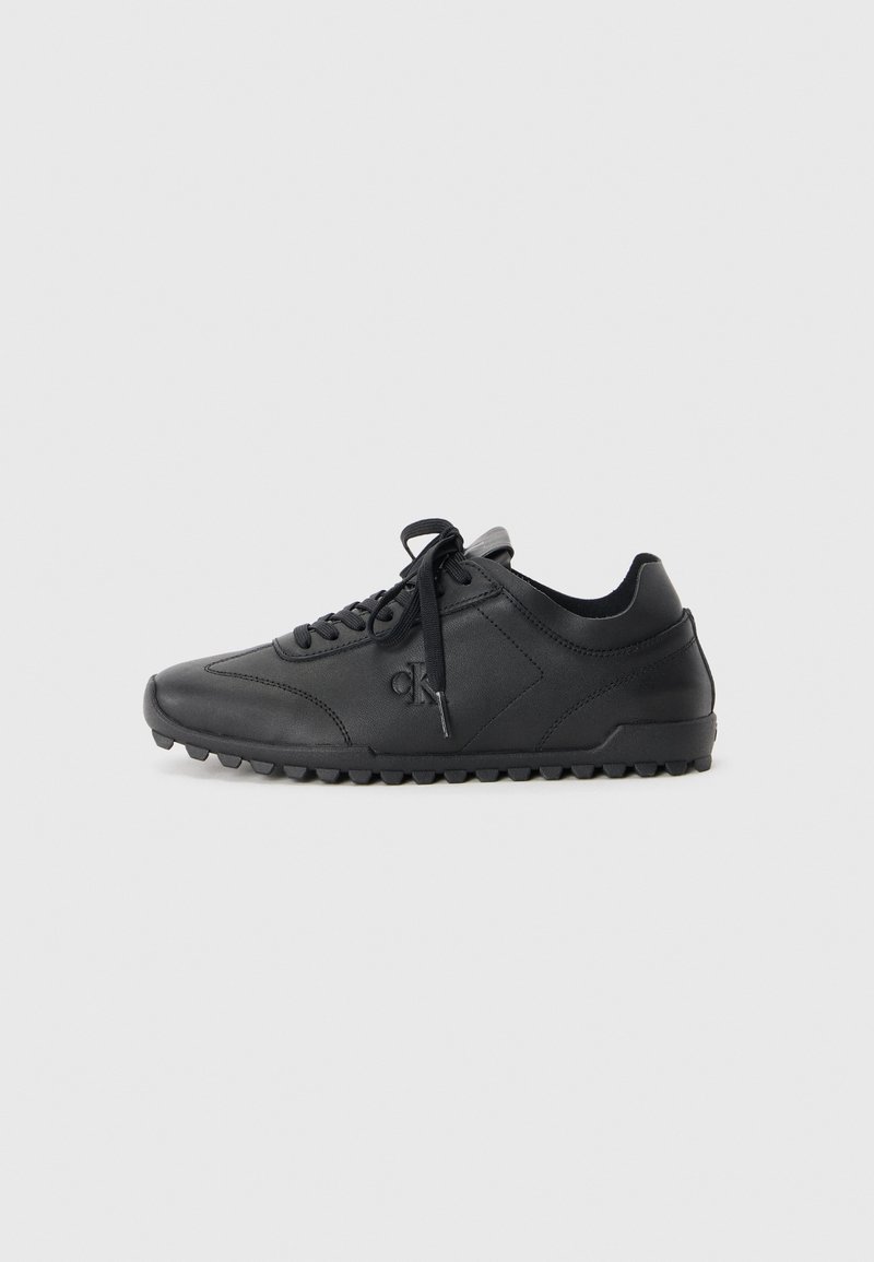 Black sneaker made of smooth leather, featuring a rounded toe, textured sole with grip, and lace-up design. Logo embossed on side.