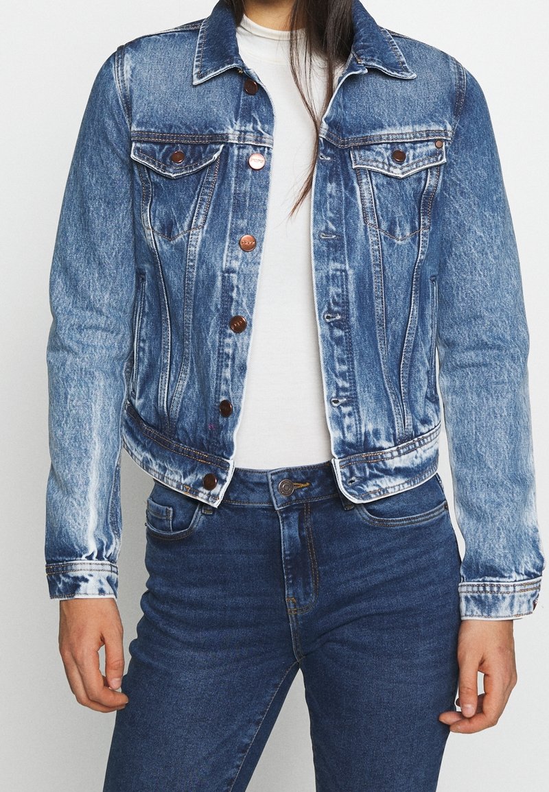 Jeanjacka i ljusblått med urtvättade detaljer, knäppning fram, bröstfickor och långa ärmar. Matchas med mörkblå jeans och vit topp.