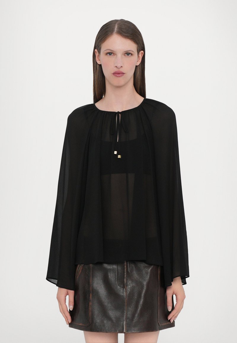 Black sheer blouse with a round neck, puff sleeves, and a tie closure, featuring two small golden accents. Paired with a metallic brown skirt.