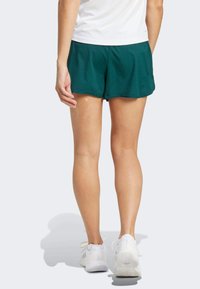 Groene sportshorts van lichtgewicht stof, met een losse pasvorm en een afgeronde zoom, gecombineerd met witte sportschoenen.