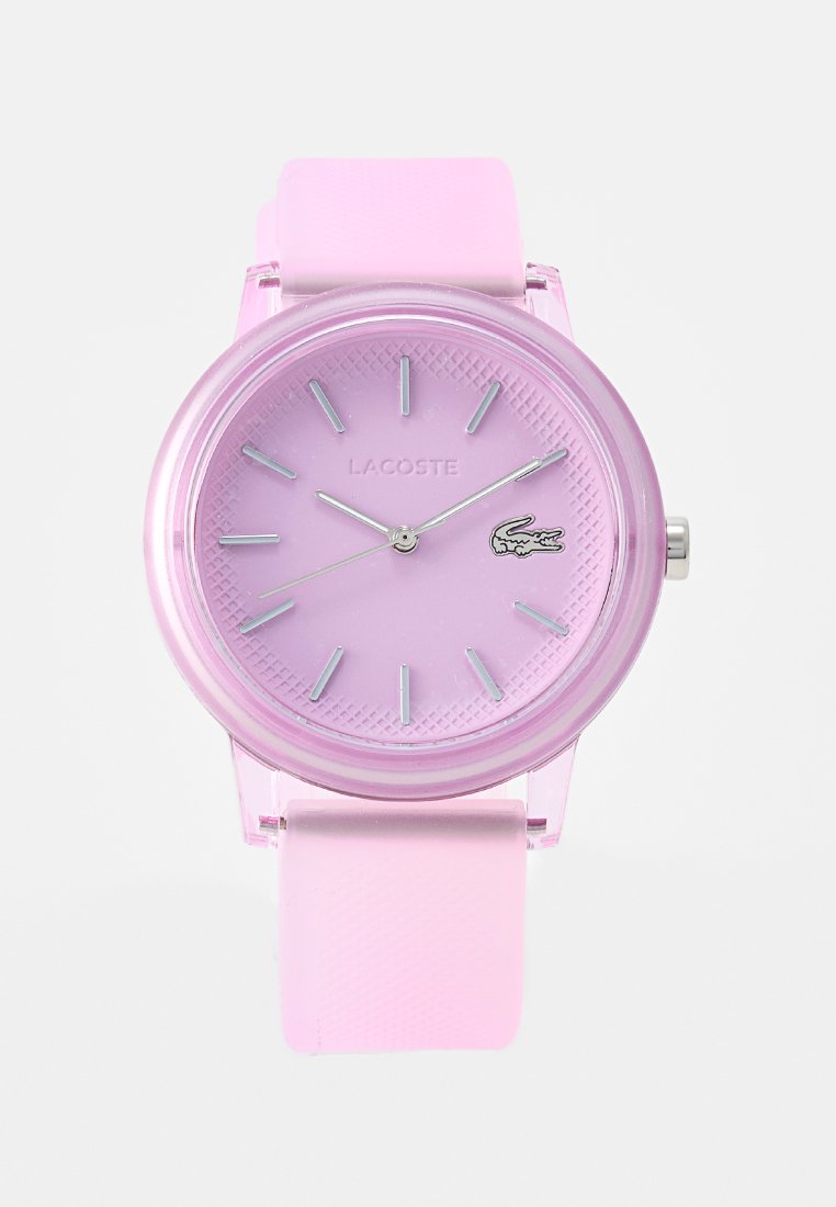 Orologio analogico rosa con cassa trasparente e cinturino in silicone abbinato. Il quadrante presenta indicatori e il logo Lacoste; motivo testurizzato sul quadrante.