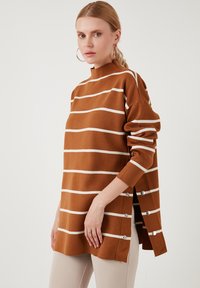 Maglione a righe marroni con strisce orizzontali bianche, collo alto, maniche lunghe e fessure laterali fissate da bottoni argentati. Texture morbida.