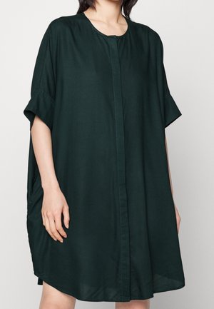 Abito verde scuro, al ginocchio, realizzato in un tessuto morbido, con scollatura tonda, maniche corte e tasche laterali. Design semplice e morbido.