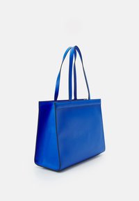 Sininen olkalaukku, joka on valmistettu sileästä materiaalista ja jolla on rakenteellinen muoto. Laukussa on kaksi pitkää kahvaa ja musta reunus saumoissa.