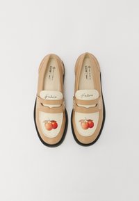 Mocassins beiges avec un panneau de couleur crème décoré d'une illustration de fruit orange. Semelle noire avec des détails de couture, et texte "J'adore" sur le dessus.