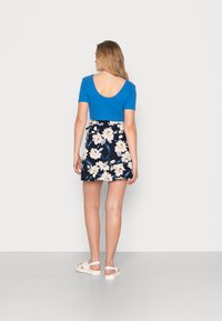 Top azul de manga curta com costas em forma de scoop, combinado com uma saia navy com padrão floral que apresenta flores brancas e rosa. Sandálias brancas com tiras.