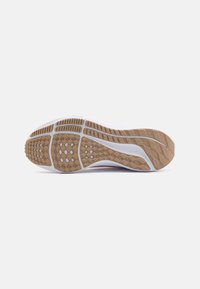 Suela de una zapatilla deportiva blanca con patrones y surcos de agarre texturizados en beige, mostrada sobre un fondo blanco liso.