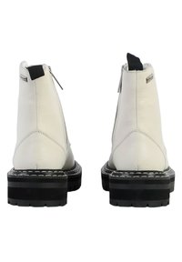 Botas de tobillo de cuero blanco con un acabado texturizado, suelas de goma negra, cierres de cremallera plateados y lengüetas negras en la parte trasera.