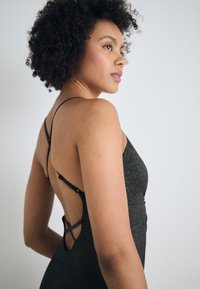 Μαύρο φόρεμα με υφή, που διαθέτει ανοιχτή πλάτη και σταυρωτές τιράντες. Το υλικό έχει μια διακριτική γυαλάδα.