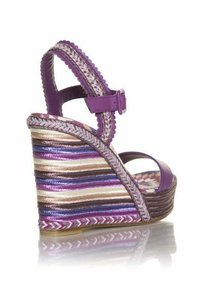 Sandalia de cuña morada con una correa trenzada y una suela de corcho a rayas multicolores, con cierre de hebilla y un diseño de punta abierta.