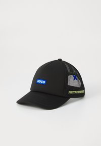 Μαύρο καπέλο με δομημένο μπροστινό μέρος, πλέγμα πίσω, μπλε λογότυπο "HUGO", πράσινο κείμενο "IGNITE THE NIGHT" και μια μικρή μπλε αστερία λεπτομέρεια στο πλάι.