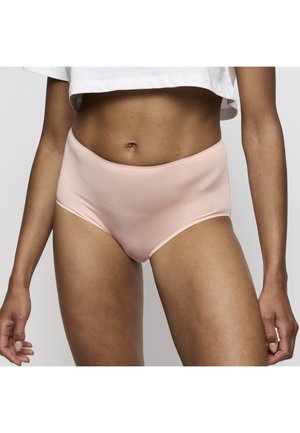Woman wearing light pink seamless high-waist underwear and a white cropped top, standing against a plain gray background.