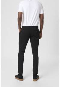Černé slim-fit kalhoty s hladkým materiálem; mají dvě zadní kapsy s knoflíky a malou akcentní visačku. Nosí se s bílým tričkem.