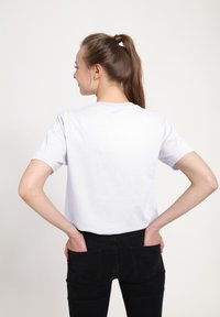 Camiseta de algodón blanca con mangas cortas y cuello redondo, combinada con pantalones de mezclilla negros. La tela parece suave y con forma ajustada.